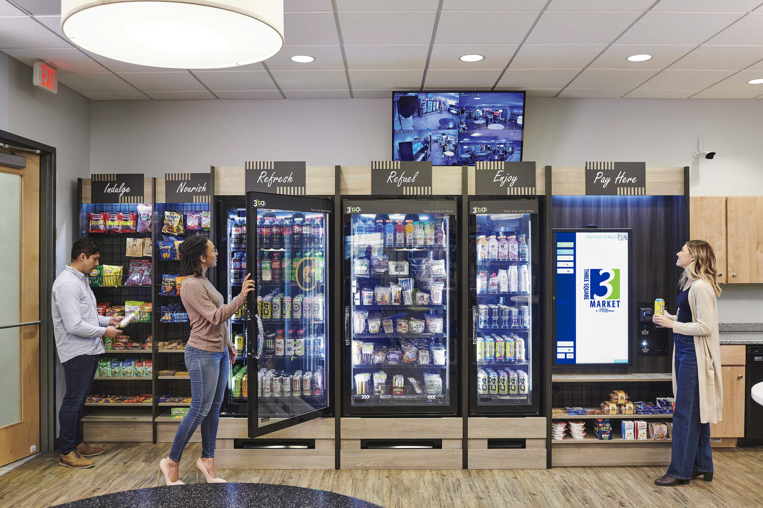 People selecting beverages and snacks from a modern micro market setup with multiple refrigerators and a digital pay station.